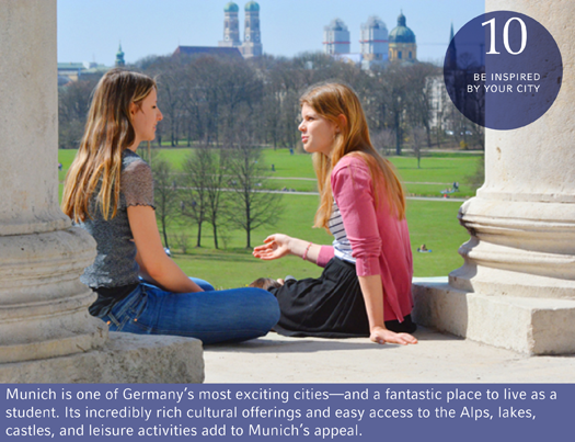 Two students sitting outdoors on the steps of a university building with historic castles in the distance.