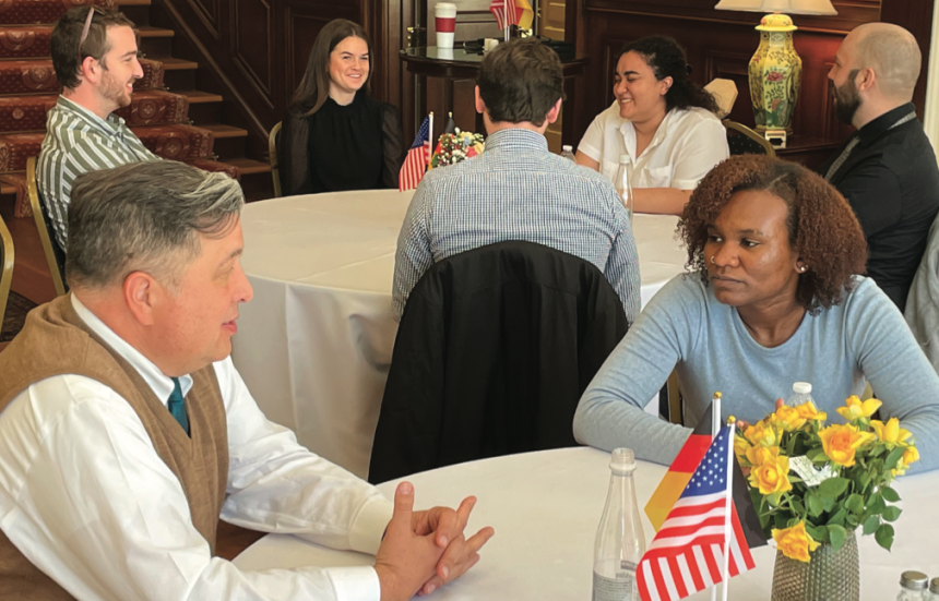 People talking at round tables with American and German flags in the center.