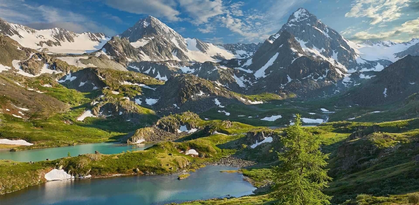 The Altai mountains--a clear blue lake sits at the mountains' feet, and green moss peaks out from under the gray, snow-capped rocks. 